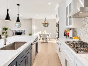 Modern white kitchen with navy island cabinetry, quartz countertops, stainless steel appliances, pendant lights, and an adjoining dining area.