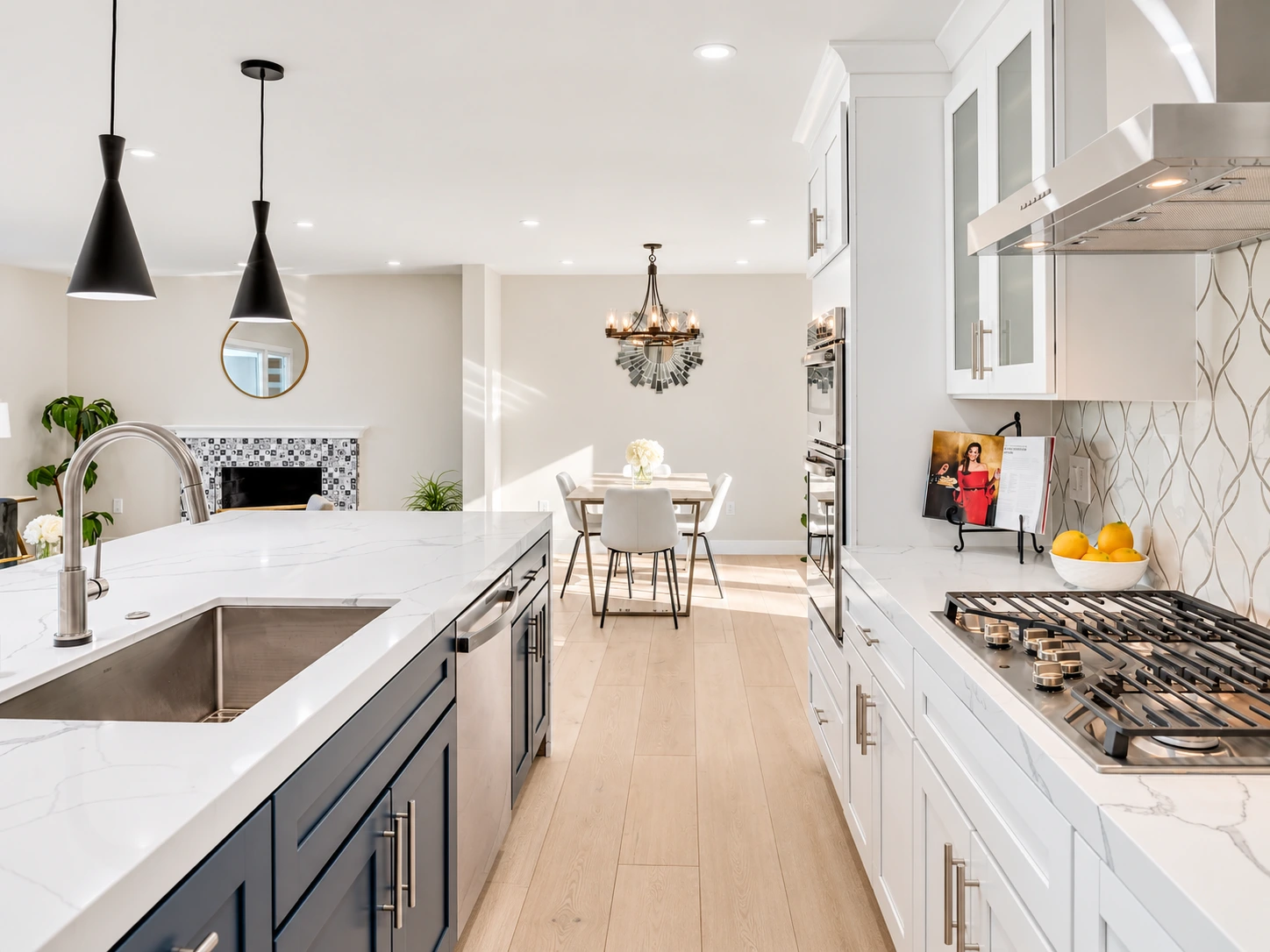 Modern white kitchen with navy island cabinetry, quartz countertops, stainless steel appliances, pendant lights, and an adjoining dining area.