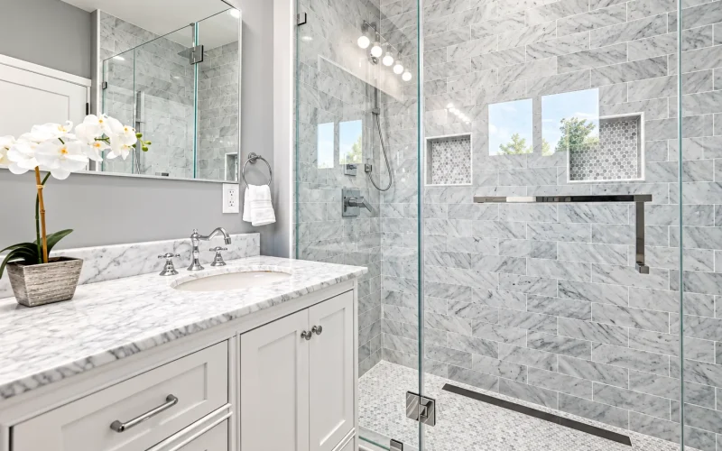 Elegant bathroom with a white marble vanity and a frameless glass shower finished with marble wall tiles and mosaic flooring.